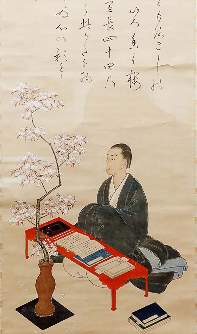 A man dressed in kimono sits at a desk where a collection of bound volumes and documents are neatly arranged. He gazes at the flowers of a potted cherry blossom tree.